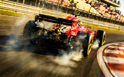 F1赛车在弯道中高速行驶，轮胎与地面摩擦产生烟雾